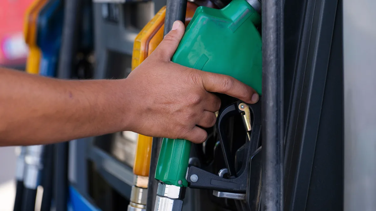 Mão segurando o bico verde de uma bomba de combustível em posto de gasolina