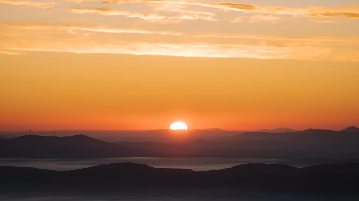 Nascer do sol sobre vales cobertos de névoa, com o céu em tons alaranjados