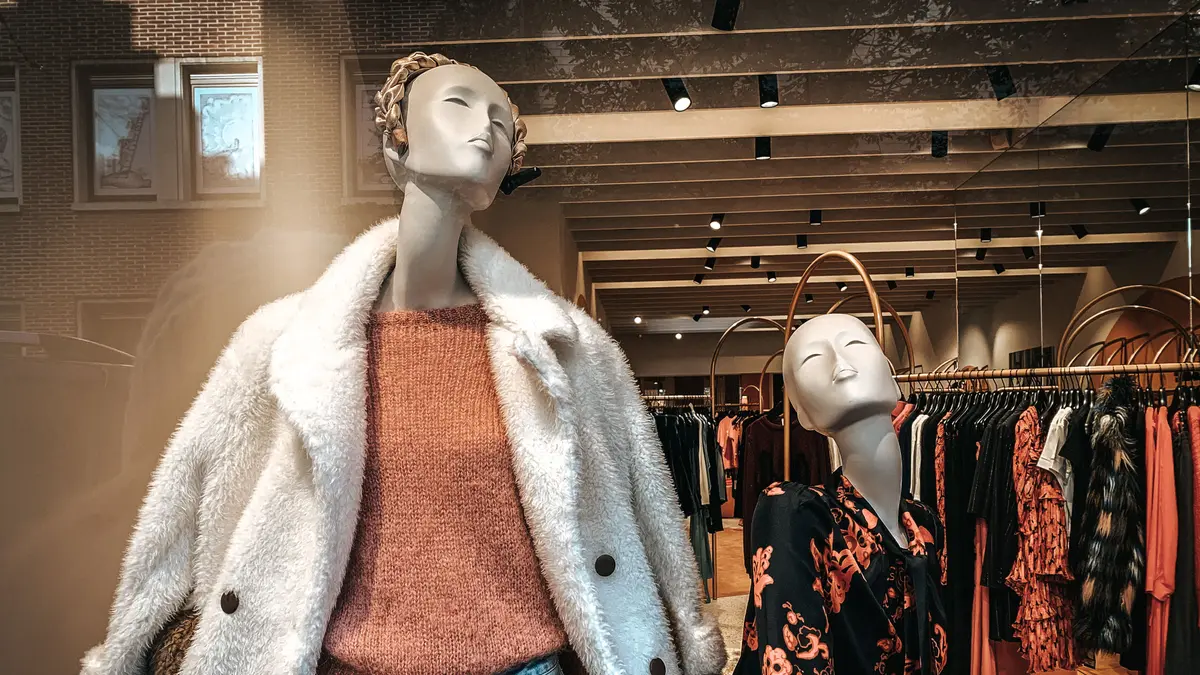 Vitrine de loja de moda com dois manequins vestidos e araras de roupas ao fundo