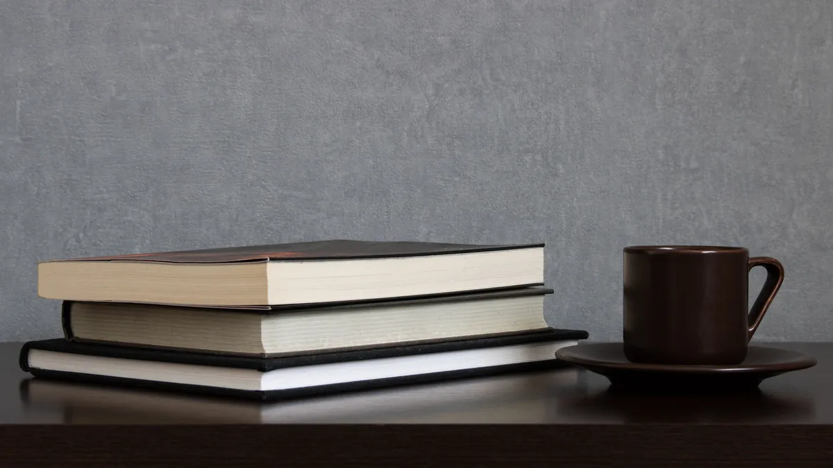 Pilha de livros ao lado de uma xícara de café sobre mesa de madeira