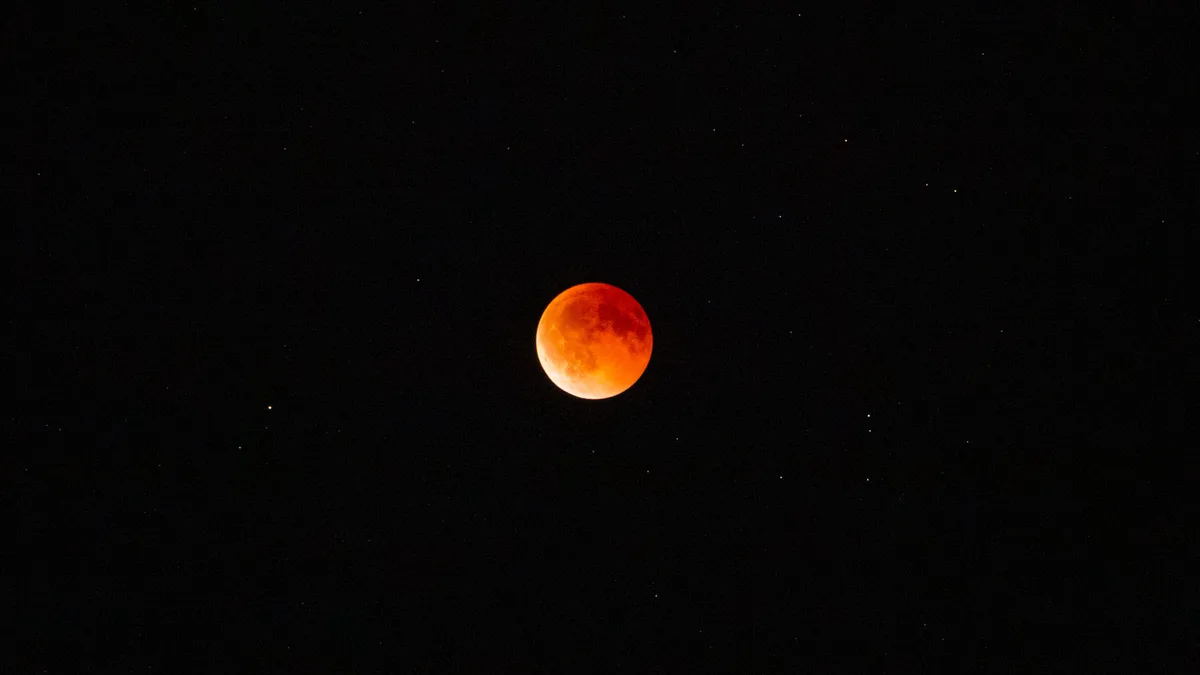 Lua totalmente eclipsada, em tom avermelhado, sobre um céu noturno estrelado