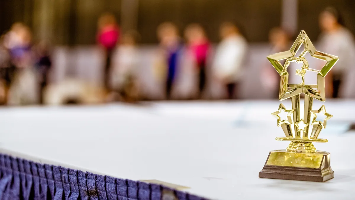 Troféu em forma de estrela sobre uma mesa, com convidados desfocados ao fundo em evento