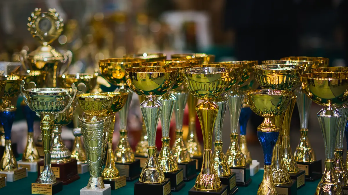 Fileira de troféus dourados sobre uma mesa, alinhados lado a lado antes de uma premiação