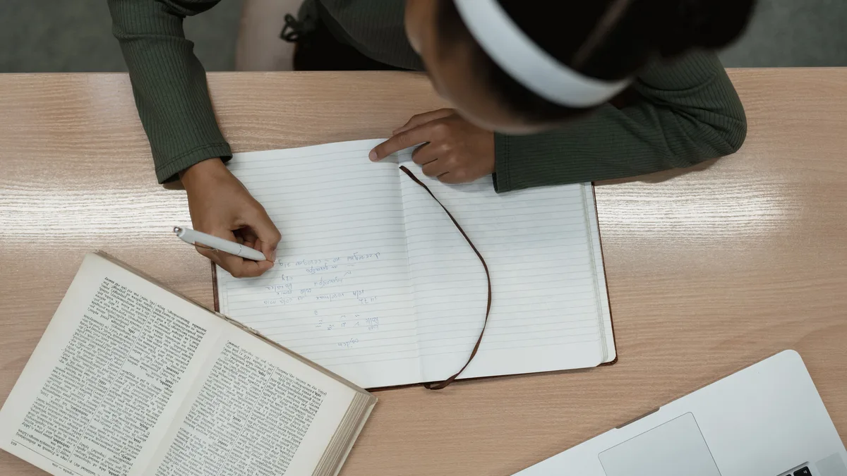 Vista de cima de pessoa estudando com livro aberto, laptop e caderno de anotações