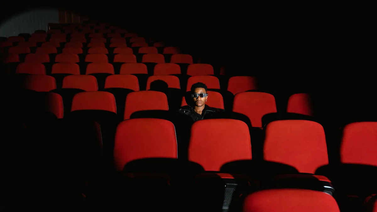 Espectador sozinho em uma sala de cinema de poltronas vermelhas, com pouca luz