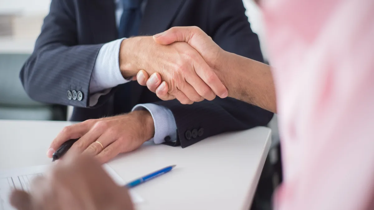 Dois executivos apertam as mãos sobre a mesa de um escritório, selando um acordo de negócios
