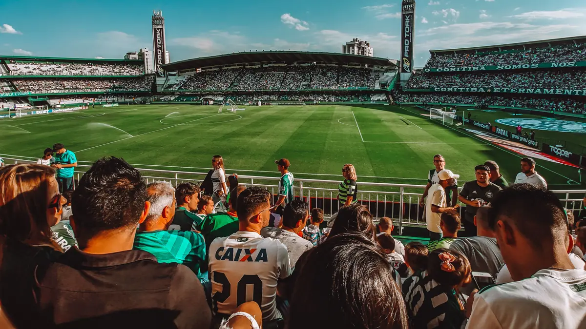 Torcida animada em estádio de futebol ensolarado, durante partida de dia