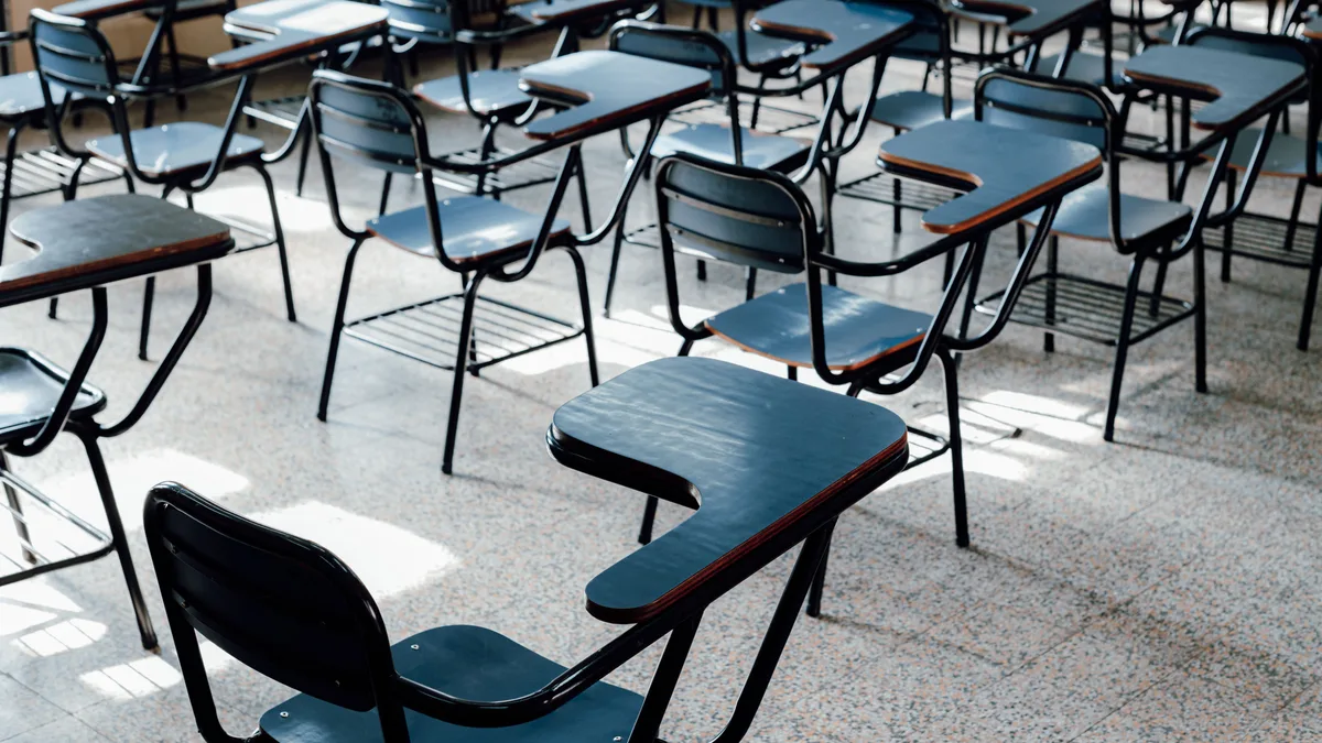 Fileiras de carteiras escolares vazias em sala de aula iluminada pela luz da janela