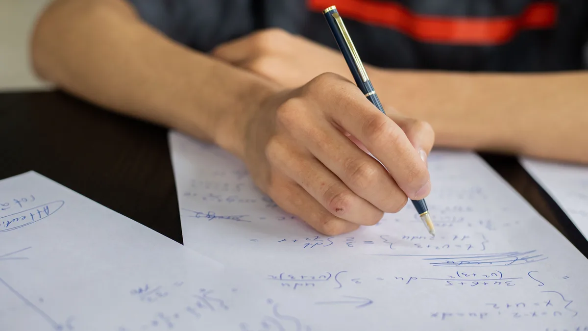 Estudante concentrado resolvendo equações de matemática no papel, com caneta na mão