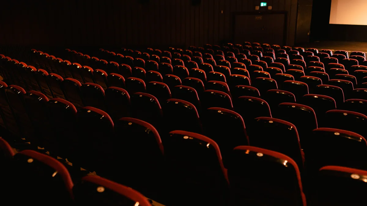 Fileiras de poltronas vermelhas vazias em sala de cinema escura