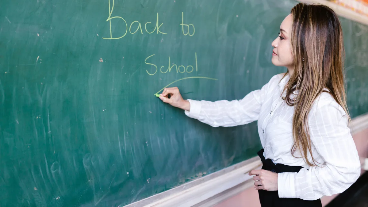 Professora escrevendo com giz em quadro-negro de sala de aula