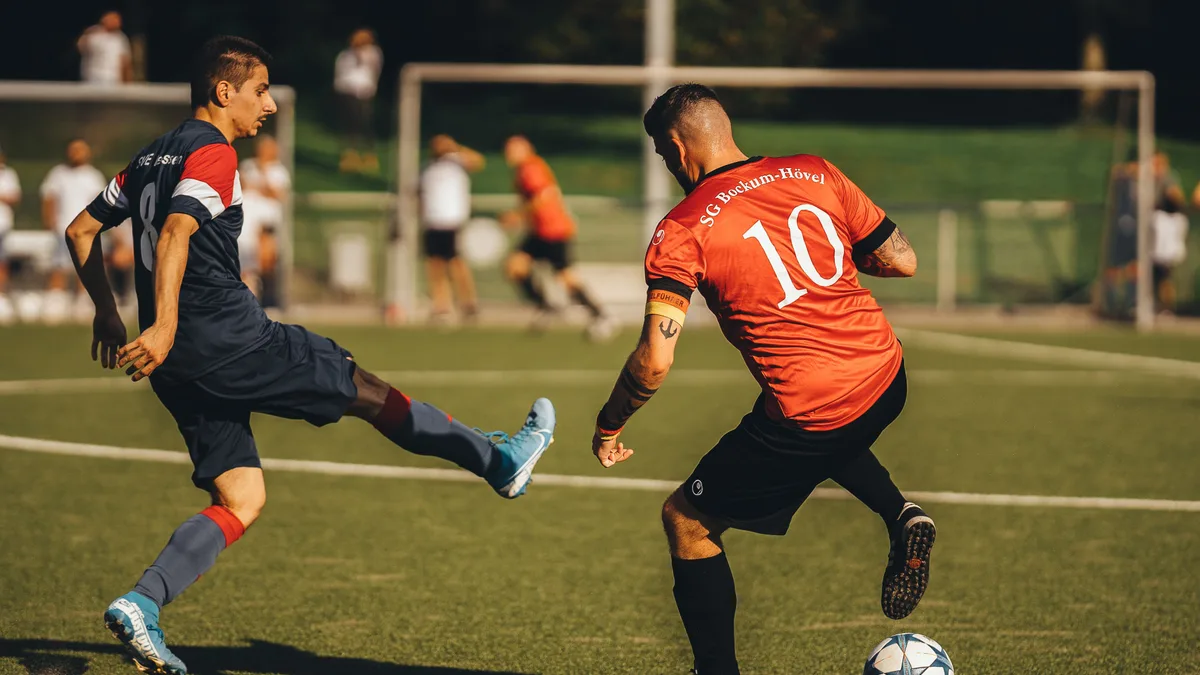 Dois jogadores de futebol disputando a bola em campo aberto, em jogada de atenção total
