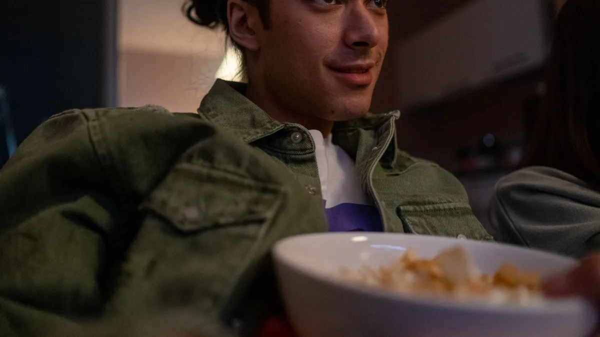 Jovem relaxando no sofá em casa, assistindo televisão e comendo petiscos