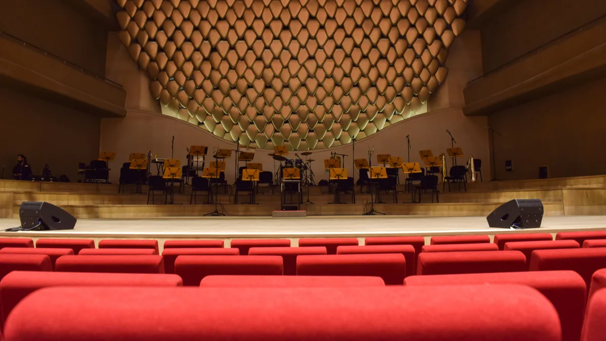 Auditório vazio, com fileiras de poltronas voltadas para o palco iluminado