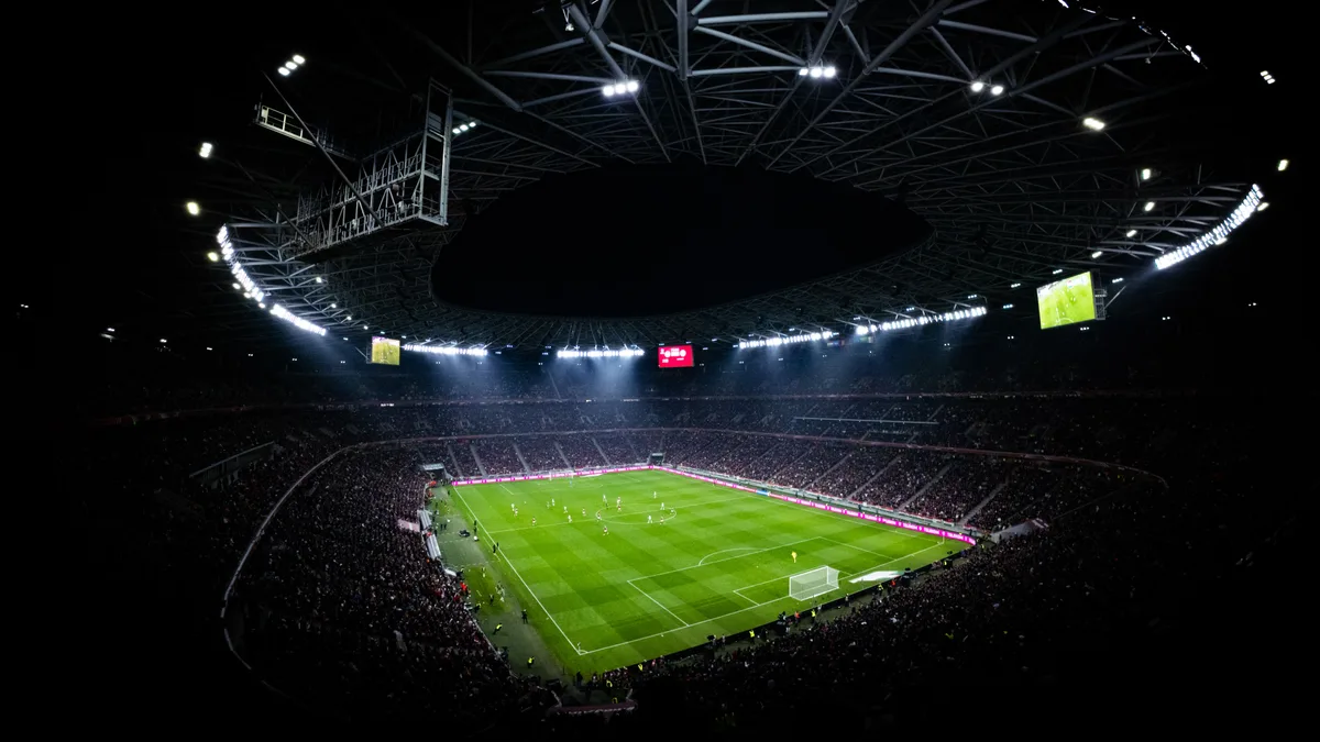 Vista aérea de estádio de futebol iluminado e lotado durante partida noturna